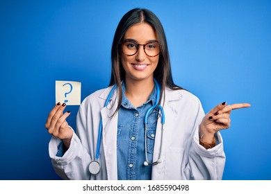 Young Beautiful Brunette Doctor Woman Holding Paper With Question Mark Symbol Message Very Happy Pointing With Hand And Finger To The Side