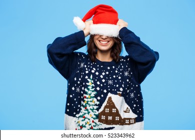 Young Beautiful Brunette Girl In Knited Sweater And Christmas Hat Smiling  Over Blue Background.