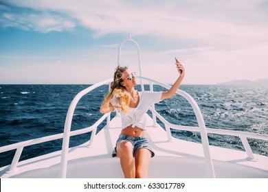 Young beautiful brunette girl making selfie using phone while sitting on the luxury yacht
