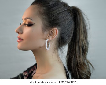 Young beautiful brunette girl, portrait in profile. Bright makeup, the hair gathered in a ponytail and Hoop earrings