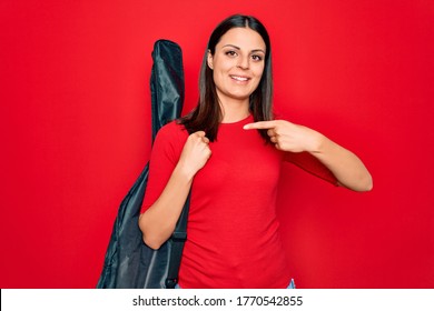 Young Beautiful Brunette Guitarist Woman Holding Guitar Case Over Isolated Red Background Smiling Happy Pointing With Hand And Finger