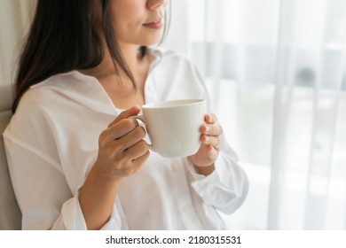 Young beautiful brunette hair woman in white shirt drinking coffee while sitting near the window in the morning. Copy space, closeup - Powered by Shutterstock