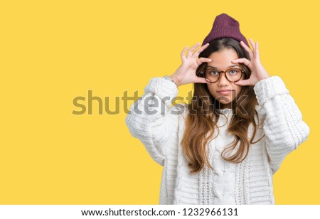 Young beautiful brunette hipster woman wearing glasses and winter hat over isolated background Trying to open eyes with fingers, sleepy and tired for morning fatigue