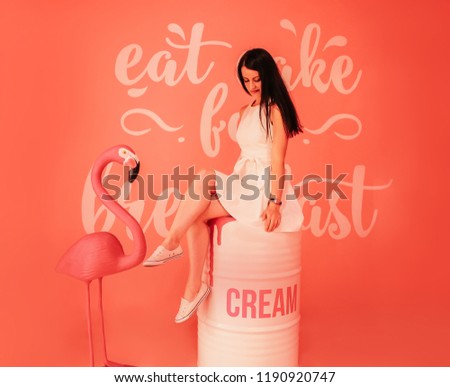 Young beautiful brunette sitting in a room with scenery on a peach background and pink flamingo