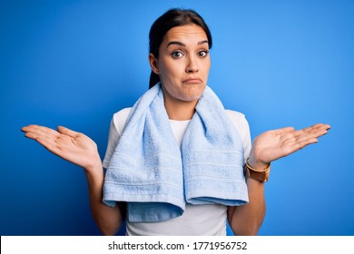 Young beautiful brunette sportswoman wearing towel doing exercise over blue background clueless and confused expression with arms and hands raised. Doubt concept. - Powered by Shutterstock