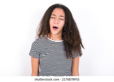 Young Beautiful Brunette Teen Girl Wearing Striped T-shirt Over White Wall Yawns With Opened Mouth Stands. Daily Morning Routine