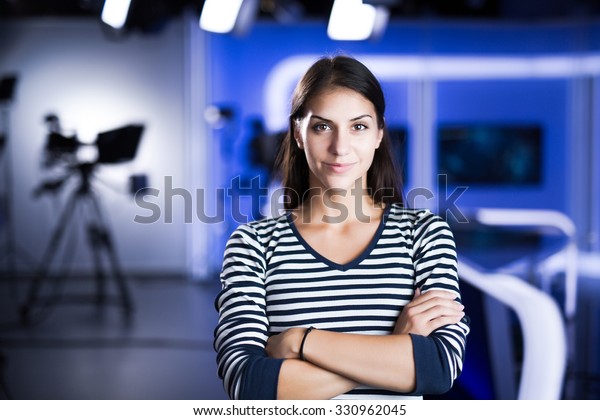 Young beautiful brunette television announcer at\
studio standing next to the camera.TV director at editor in\
studio.Recording at TV studio with television anchorwoman. TV NEWS\
studio behind the scenes