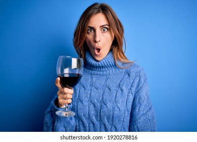 Young beautiful brunette woman drinking glass of red wine over isolated blue background scared in shock with a surprise face, afraid and excited with fear expression