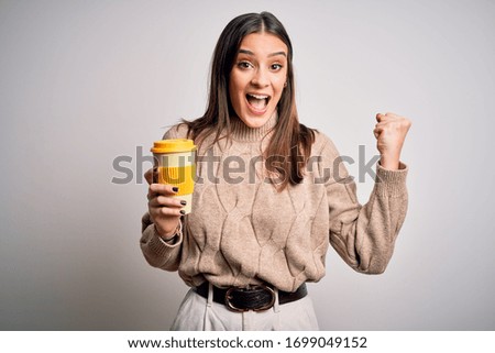 Young beautiful brunette woman drinking glass of coffee over isolated white background screaming proud and celebrating victory and success very excited, cheering emotion