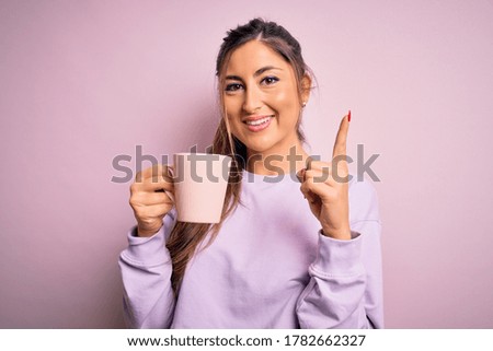 Young beautiful brunette woman drinking mug of coffee over isolated pink background surprised with an idea or question pointing finger with happy face, number one