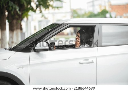 young beautiful brunette woman driver sitting in her car with a glass of coffee and talking on the phone