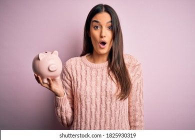 Young Beautiful Brunette Woman Holding Piggy Bank Saving Money For Retirement Scared In Shock With A Surprise Face, Afraid And Excited With Fear Expression