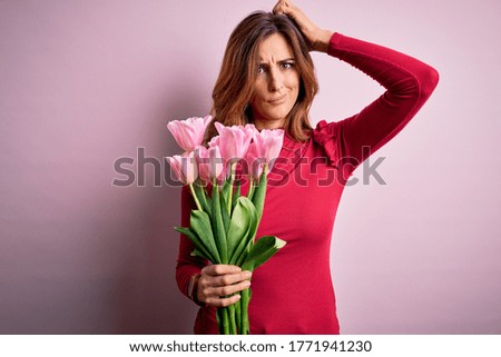 Young beautiful brunette woman holding bouquet of pink tulips over isolated background confuse and wondering about question. Uncertain with doubt, thinking with hand on head. Pensive concept.