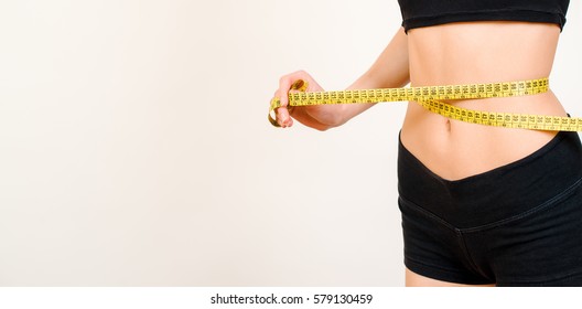 Young beautiful brunette woman measuring her waist with a measure tape isolated on a white background.