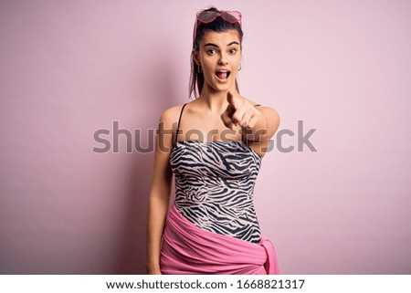 Young beautiful brunette woman on vacation wearing swimsuit over pink background pointing displeased and frustrated to the camera, angry and furious with you