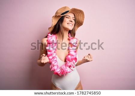 Young beautiful brunette woman on vacation wearing swimsuit and Hawaiian flowers lei excited for success with arms raised and eyes closed celebrating victory smiling. Winner concept.