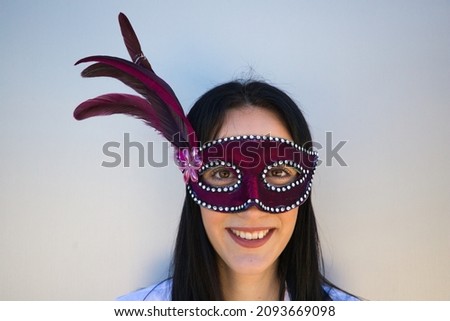 Young and beautiful brunette woman with a purple carnival mask with rhinestones and feathers on a white background. The woman makes different expressions. Carnival mask and costume concept.