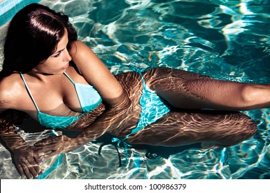 young beautiful brunette woman resting in the swimming pool on the sunny day