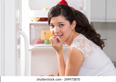 young beautiful brunette woman searching for food in the fridge looking nervous