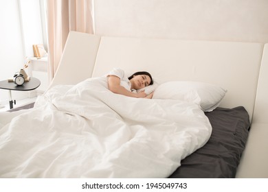 Young beautiful brunette woman sleeping peacefully in large comfortable double bed under white blanket with her head on soft pillow