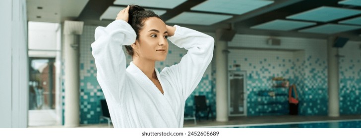 A young, beautiful brunette woman standing gracefully by an indoor swimming pool, exuding serenity and tranquility. - Powered by Shutterstock