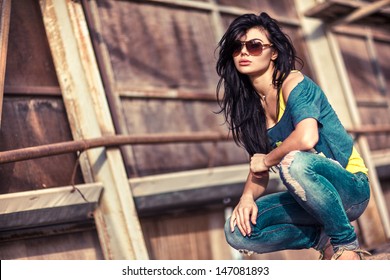 Young beautiful brunette woman in sunglasses sitting behind texture wall.