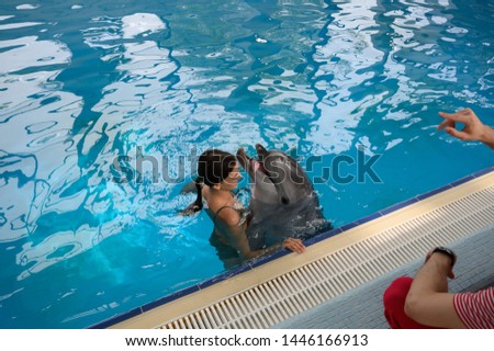 young beautiful brunette woman in a swimsuit swims and plays with a funny cute sea dolphin. Emotional rest in the water park. positive emotions, communication with marine mammals