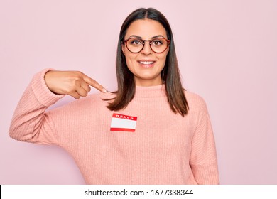 Young beautiful brunette woman wearing sticker with hello my name is message pointing finger to one self smiling happy and proud
