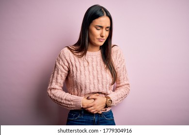 Young beautiful brunette woman wearing casual sweater over isolated pink background with hand on stomach because indigestion, painful illness feeling unwell. Ache concept.
