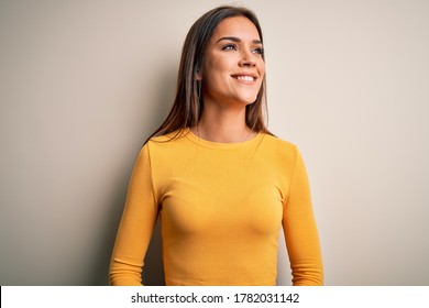 Young Beautiful Brunette Woman Wearing Yellow Casual T-shirt Over White Background Looking Away To Side With Smile On Face, Natural Expression. Laughing Confident.