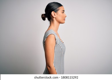 Young beautiful brunette woman wearing casual striped dress over isolated white background looking to side, relax profile pose with natural face with confident smile.