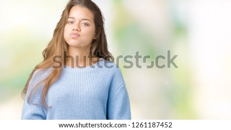 Young beautiful brunette woman wearing blue winter sweater over isolated background puffing cheeks with funny face. Mouth inflated with air, crazy expression.