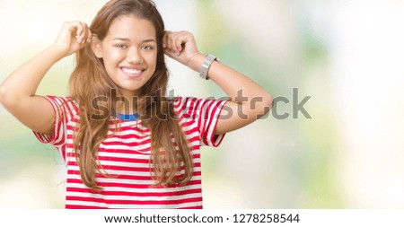 Young beautiful brunette woman wearing stripes t-shirt over isolated background Smiling pulling ears with fingers, funny gesture. Audition problem