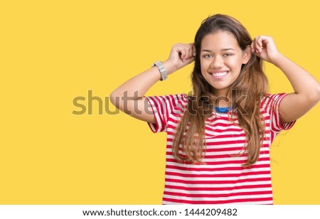 Young beautiful brunette woman wearing stripes t-shirt over isolated background Smiling pulling ears with fingers, funny gesture. Audition problem