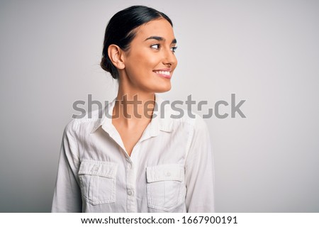 Young beautiful brunette woman wearing casual shirt over isolated white background looking away to side with smile on face, natural expression. Laughing confident.