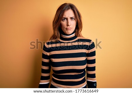 Young beautiful brunette woman wearing striped turtleneck sweater over yellow background depressed and worry for distress, crying angry and afraid. Sad expression.