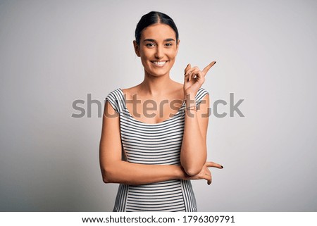 Young beautiful brunette woman wearing casual striped dress over isolated white background with a big smile on face, pointing with hand and finger to the side looking at the camera.