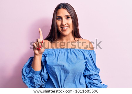 Young beautiful brunette woman wearing casual t-shirt smiling with an idea or question pointing finger up with happy face, number one 