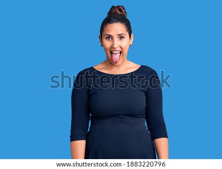 Young beautiful brunette woman wearing casual dress sticking tongue out happy with funny expression. emotion concept. 