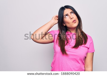 Young beautiful brunette woman wearing casual pink t-shirt standing over white background confuse and wondering about question. Uncertain with doubt, thinking with hand on head. Pensive concept.