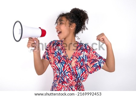 young beautiful brunette woman wearing colourful dress over white wall communicates shouting loud holding a megaphone, expressing success and positive concept, idea for marketing or sales.