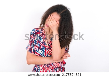 young beautiful brunette woman wearing colourful dress over white wall making facepalm gesture while smiling amazed with stupid situation.