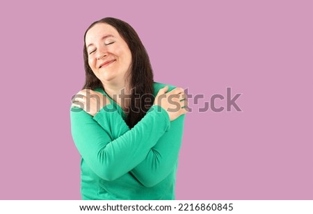 Young beautiful brunette woman wearing casual t-shirt standing over pink background Hugging oneself happy and positive, smiling confident. Self love and self care