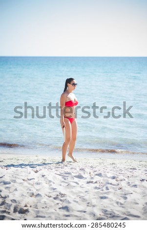 young beautiful brunette woman wearing swimsuit and sunglasses in summertime at the beach with racket
