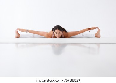 Young Beautiful Brunette Woman Yoga Instructor Doing Twine And Stretching Exercise Lying On Floor On White Isolated Background