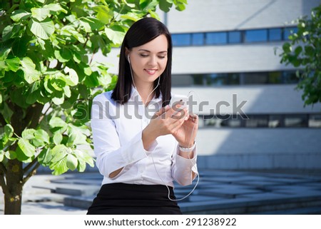 young beautiful business woman listening music with smartphone in city park