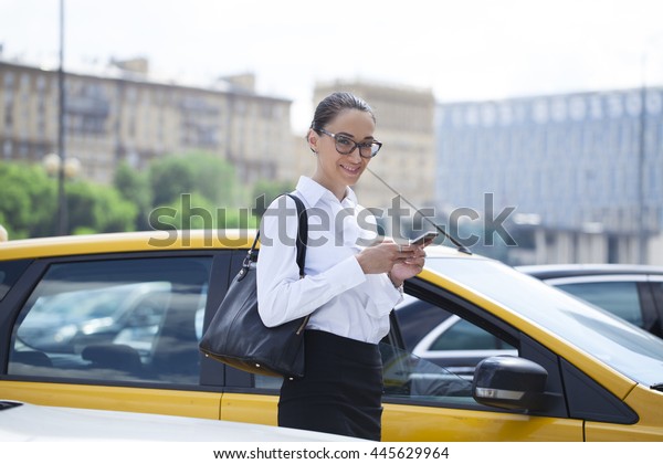 Young beautiful business woman with\
phone on a background of yellow taxis in the city\
center