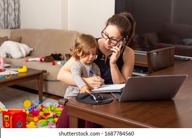 Young Beautiful Business Woman Talking On Mobile Phone And Working On A Laptop. Mother Playing With Child During Working. Women Powerful. Lady Working At Home During Quarantine Because Of Coronavirus.