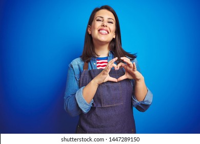 Young beautiful business woman wearing store uniform apron over blue isolated background smiling in love showing heart symbol and shape with hands. Romantic concept.