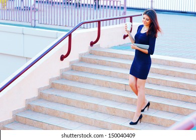Young beautiful businesswoman going down the stairs with coffee and tablet computer